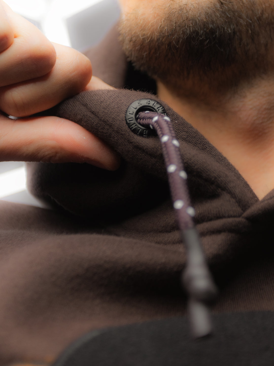 Detailaufnahme der Metallösen mit eingestanztem CLRBLND-Logo für die Kordel des Falling Leaves Teddy Hoodies.