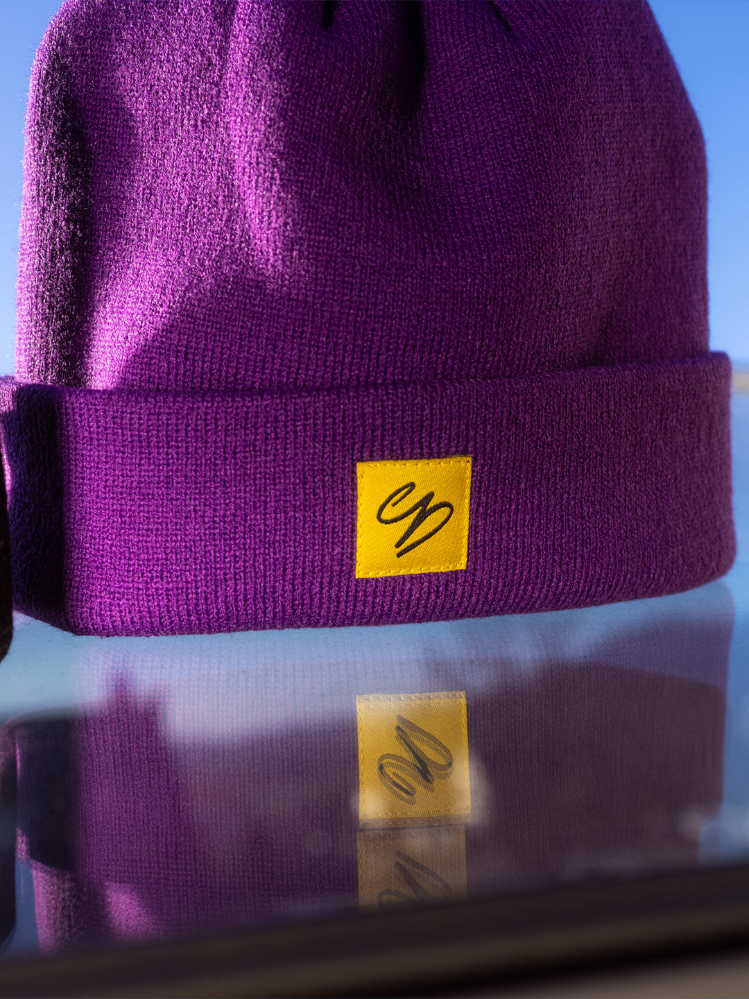 Detailaufnahme der lila Winter Beanie mit gelbem Webpatch und hochwertiger Verarbeitung